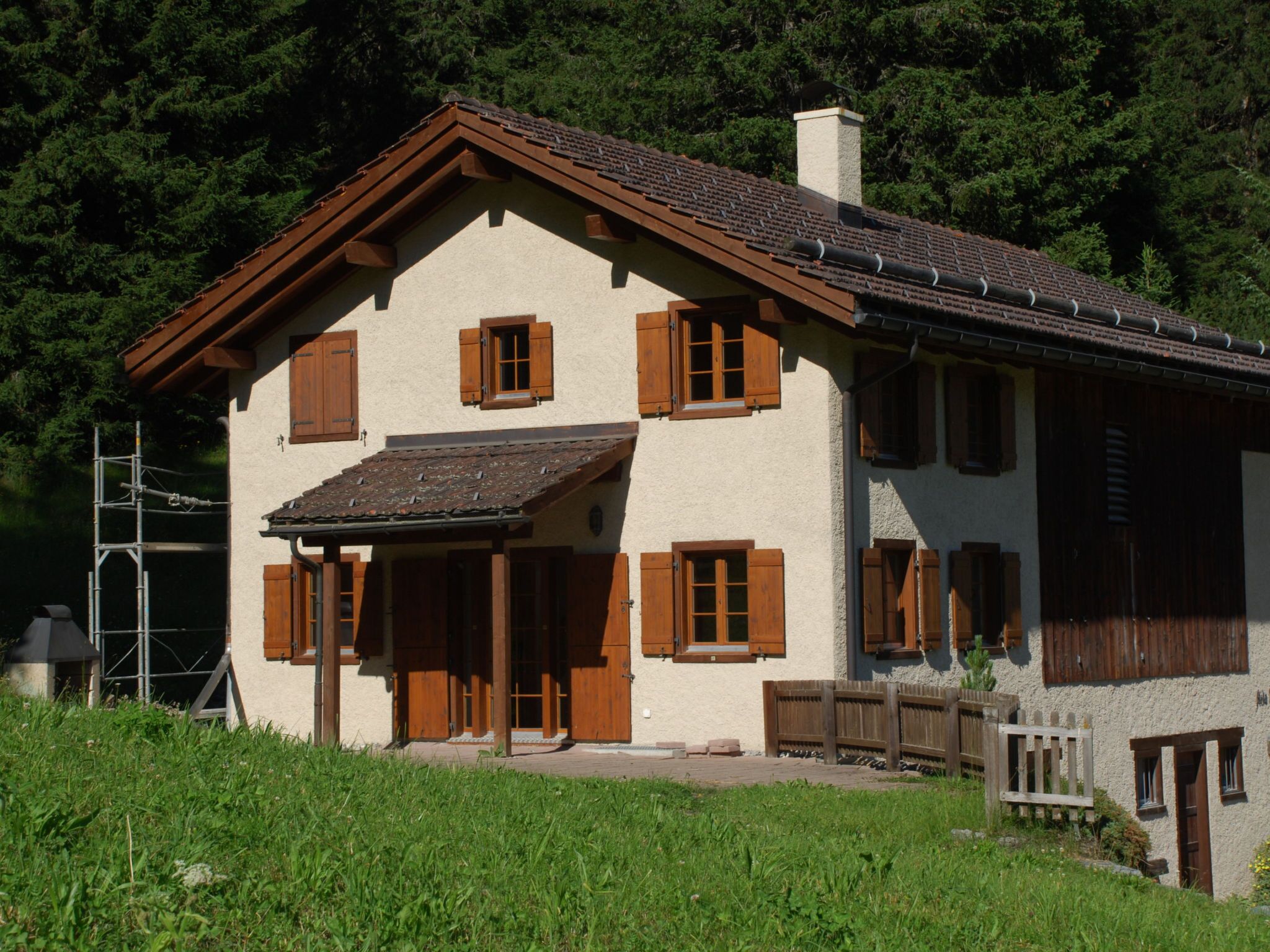 Une maison à deux étages, dotée d’un toit en pente, de volets en bois et d’une cheminée.