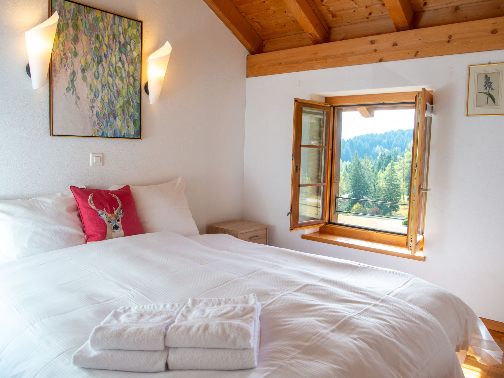 Een slaapkamer met een groot bed, een nachtkastje, een raam met open luik en een schilderij aan de muur.
