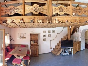 Um interior rústico com teto de madeira, área de refeições com almofadas vermelhas, televisão e escada.