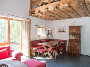 Uma área de refeições com mesa e cadeiras de madeira, um banco, um armário e uma janela com cortinas.