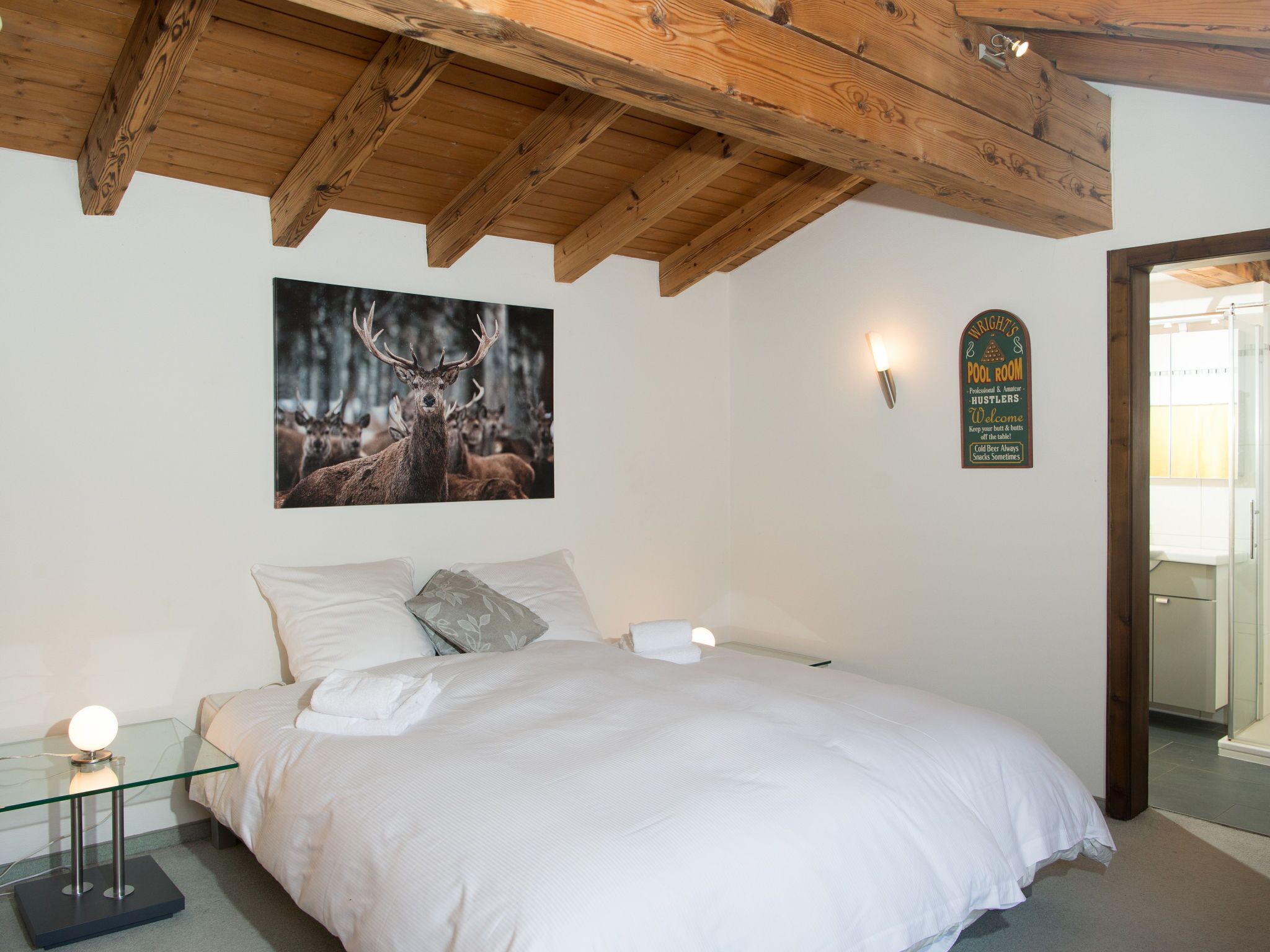 Ein Schlafzimmer mit einem großen Bett, einem Hirschgemälde, einem Schild und einem Glastisch mit einer Lampe.