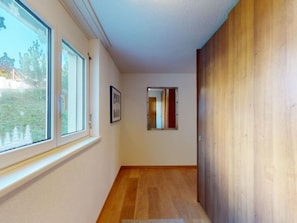 A hallway with wooden flooring, a window, and a door.
