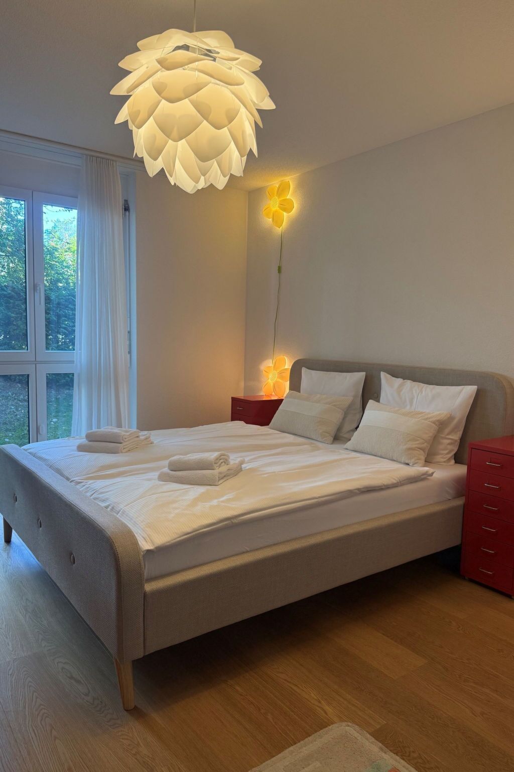 Ein modernes Schlafzimmer mit einem großen Bett, einem roten Nachttisch und einer außergewöhnlichen Deckenleuchte.