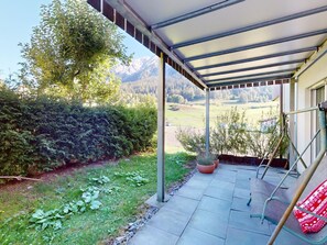 Eine überdachte Terrasse mit Blick auf eine gebirgige Landschaft, ein Sitzbereich mit Tisch und Stühlen und Kübelpflanzen.