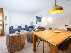 Hyggelig opholdsstue med sofa, to fletpuder, et træspisebord og en hængende lampe.