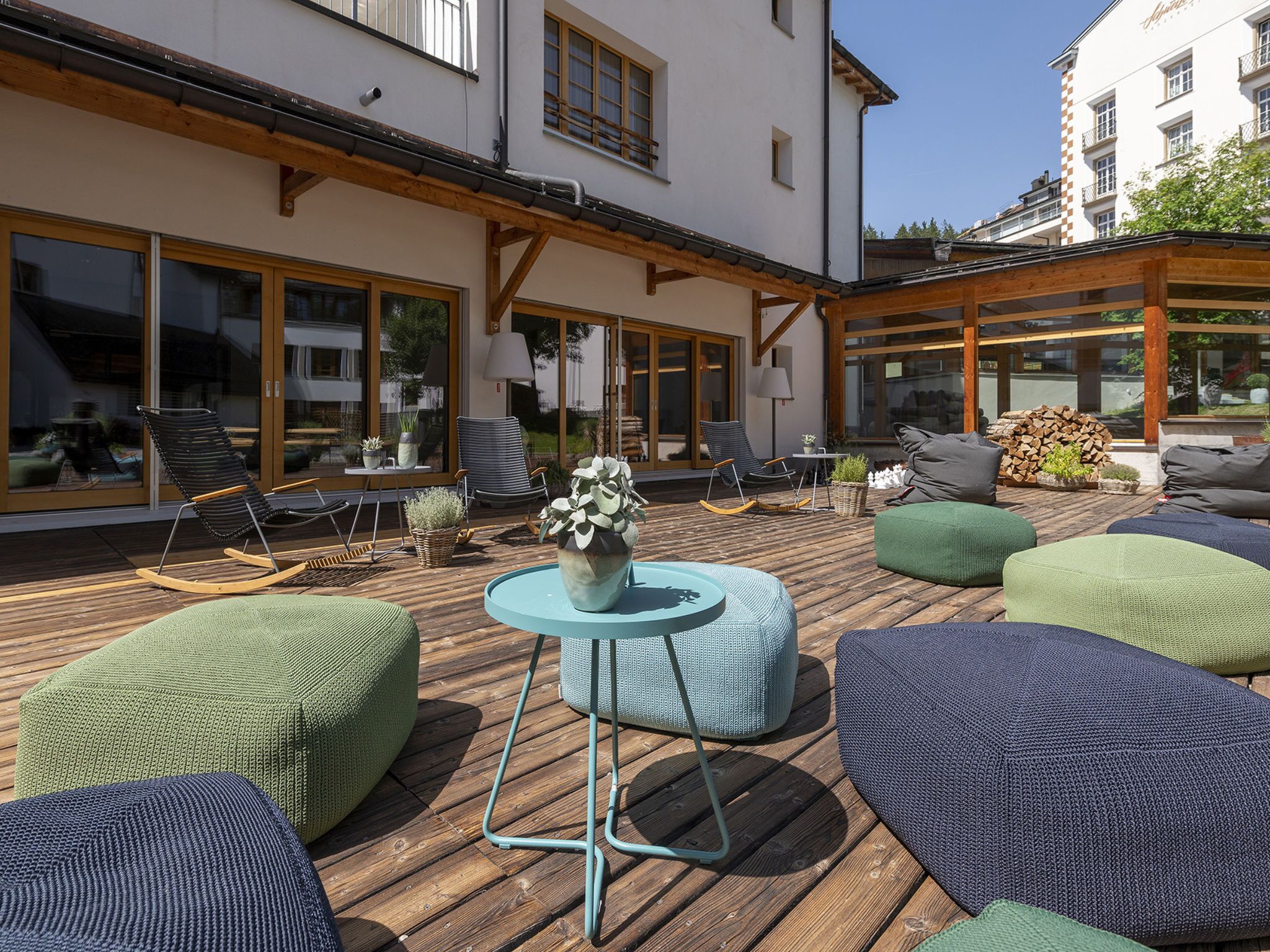 An outdoor patio with wooden flooring, cushioned seating, and a central table.