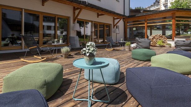 An outdoor patio with wooden flooring, cushioned seating, and a central table. - 1620 Schweizerhof 402 by Interhome (Lenzerheide)
