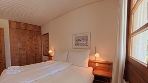 A bedroom with a large bed, wooden wardrobe, bedside lamps, and a framed picture on the wall. - 1620 Schweizerhof 402 by Interhome (Lenzerheide)