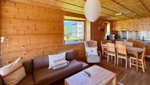 L’intérieur d’un chalet en bois comprend un canapé, une table à manger, des chaises et un coin cuisine.