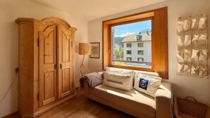 Une pièce avec une armoire en bois, un canapé avec des coussins, une lampe et une fenêtre donnant sur des immeubles.