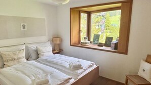 Une chambre à coucher avec un grand lit, une fenêtre donnant sur un beau paysage, une table de chevet et une chaise.