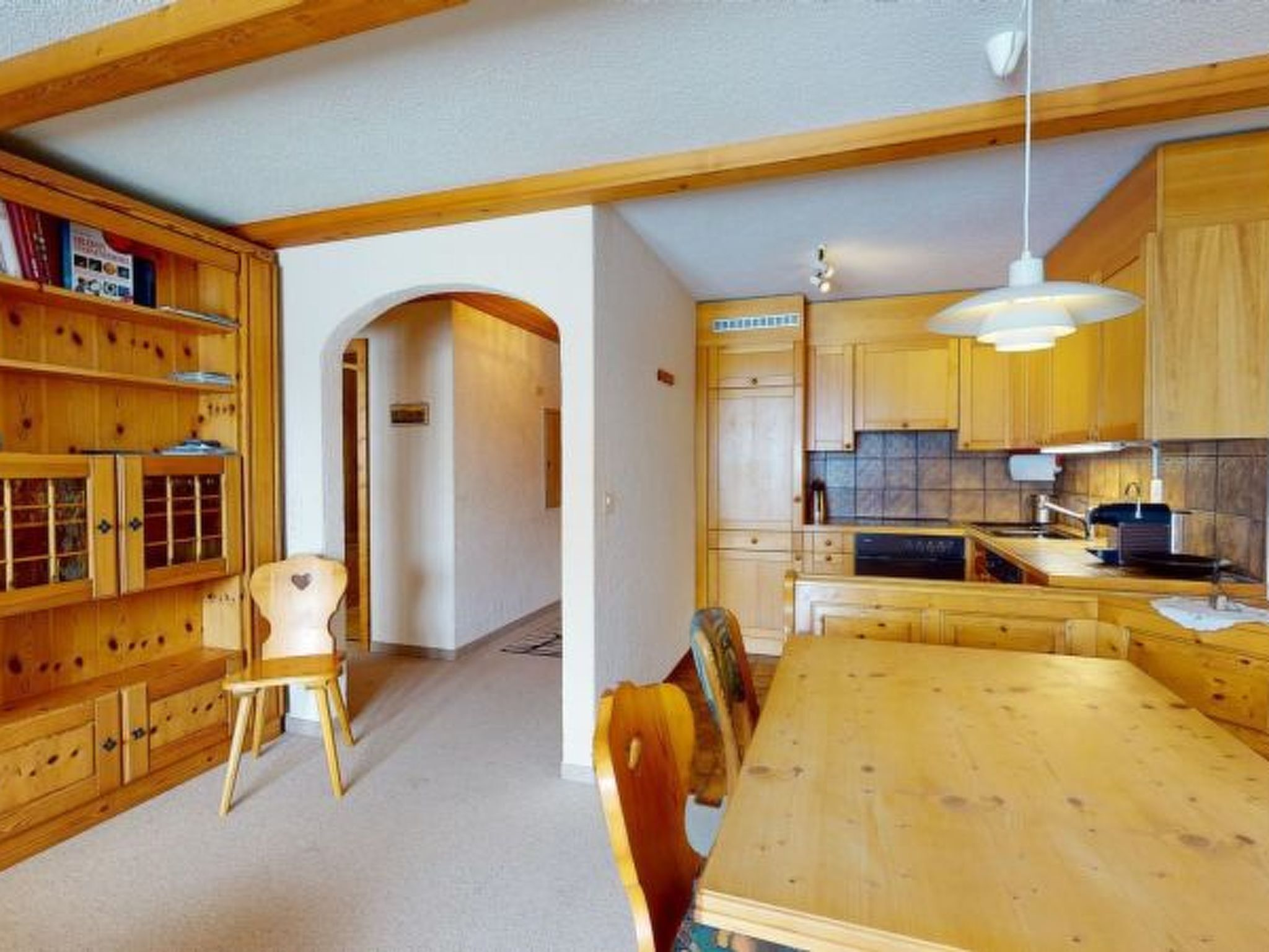 A wooden interior with a dining table, chairs, a kitchen area, and built-in shelving.