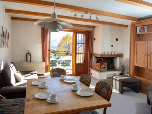 A dining area with a wooden table set for four, a sofa, and a view of the outdoors through a large window. - Arnika Family Accommodation in Lantsch-Lenz – For 5 People by Interhome (Lantsch)