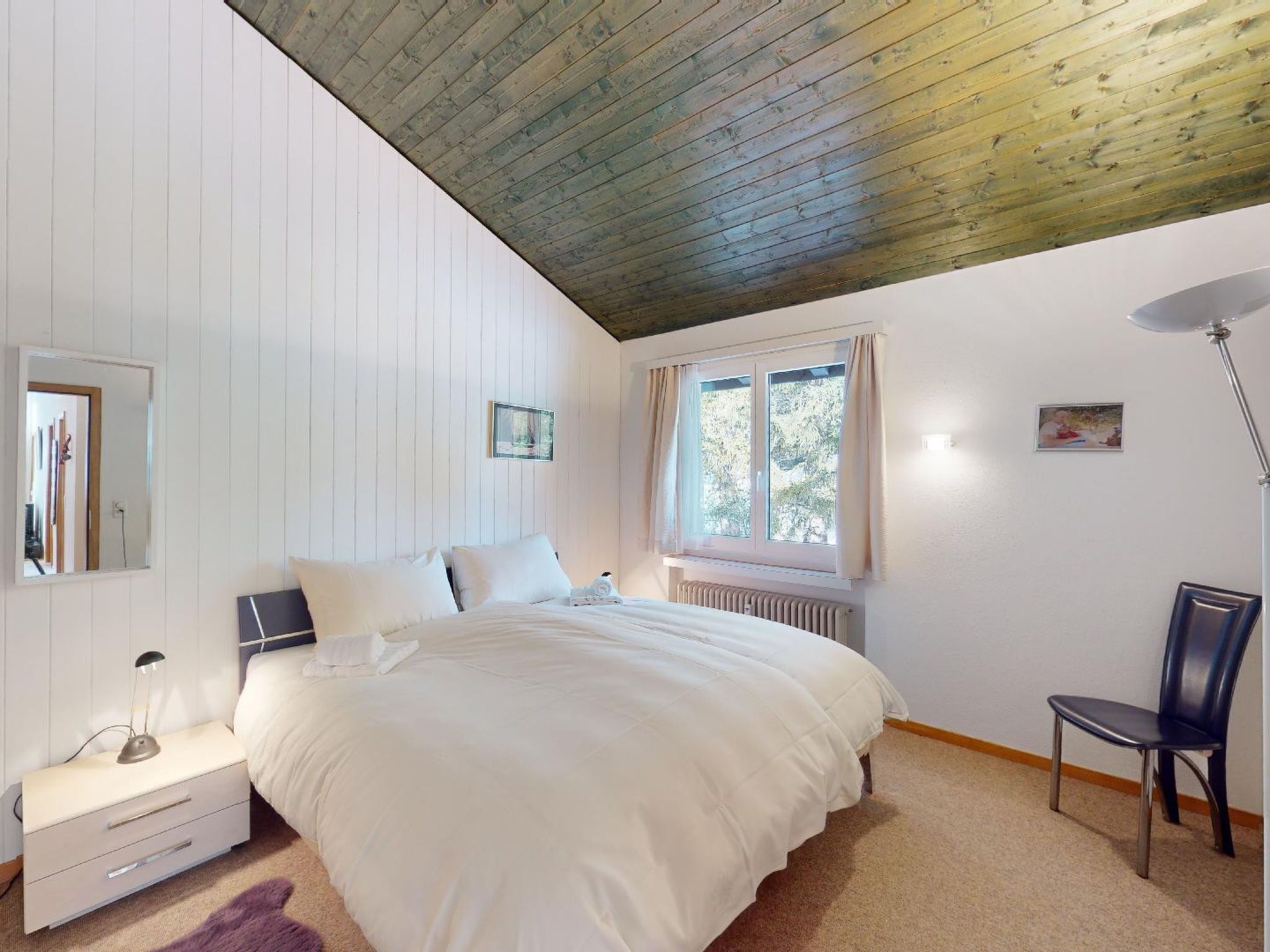 Ein Schlafzimmer mit einem Bett, einem Nachttisch, einem Sessel, einem Fenster und einer Heizung.