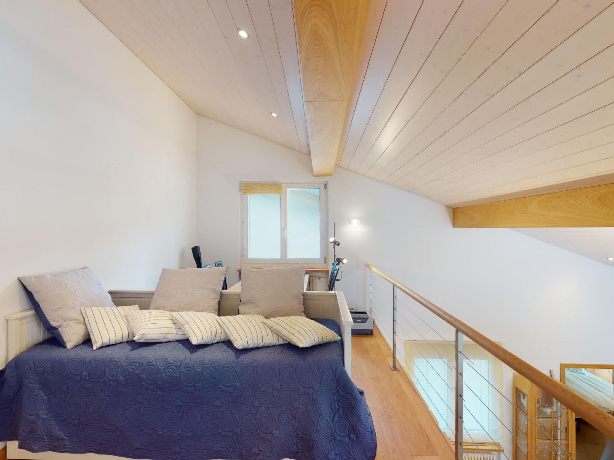 Un dormitorio con una cama grande, una mesita de noche, una lámpara y vista al piso superior.