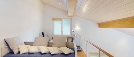 Et soveværelse med en stor seng, et natbord, en lampe og udsigt til et øvre etage.