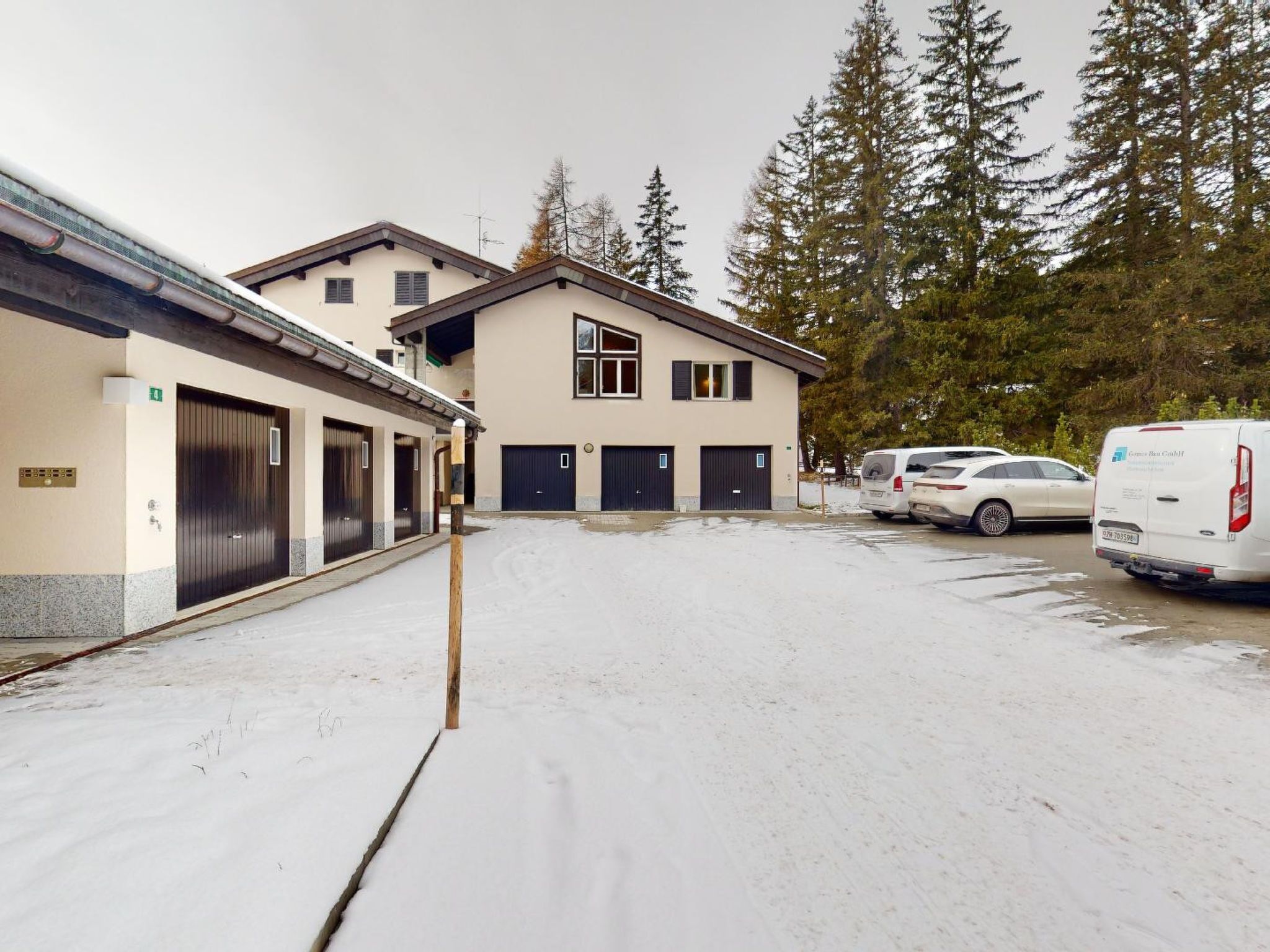 Ein Gebäude mit mehreren Garagentoren, einem Parkplatz mit zwei weißen Fahrzeugen und einem schneebedeckten Gelände.
