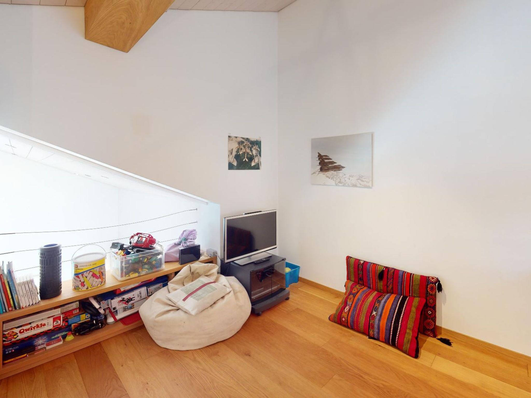 Un espacio de estar pequeño con televisión, sillón de mimbre, estantería y ventana.
