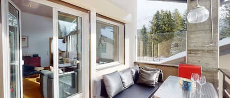A modern living space with a glass door leading to a kitchen, a dining area with a table and chairs, and a seating area with a bench.