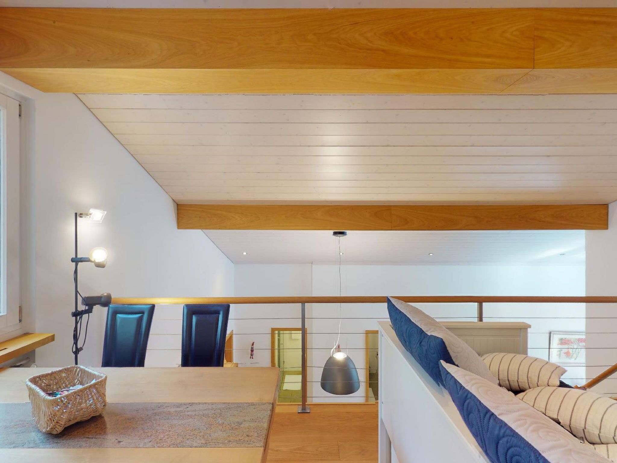 Ein modernes Interieur mit Holzboden, einer Treppe, einem Sofa und einer hängenden Leuchte.