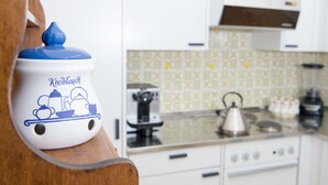 Una cocina con armarios blancos, un salpicadero estampado y una tetera azul y blanca sobre una repisa de madera.