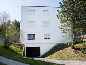 A modern two-story building with a flat roof, a garage, and a small front yard with a tree. - 1603 Sundrella by Interhome (Lenzerheide)
