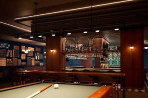 A pool table with a billiard cue and balls, a bar area with bottles, and a wall with framed pictures. - Hyatt Vivid Punta Cana Adults Only (Punta Cana)