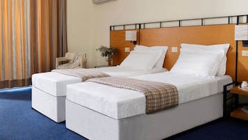 A hotel room with two beds, a wooden headboard, a bedside table with a telephone, and a chair.