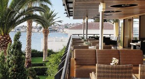 A terrace with wicker furniture, a view of the sea, and a cityscape in the background. - Spetses (Spetses)