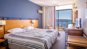 Una habitación de hotel con una cama, un escritorio, una silla y vista al mar.