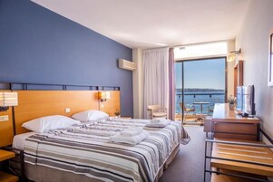 A hotel room with a bed, a desk, a chair, and a view of the sea.