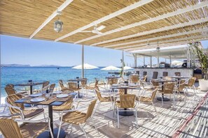 An outdoor dining area with tables and chairs, a view of the sea, and umbrellas. - Spetses (Spetses)