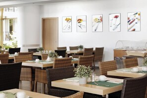 A dining area with wicker chairs, tables set with white teacups, and framed pictures on the wall. - Spetses (Spetses)