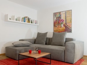 Un salon moderne avec un canapé gris, une table basse, des tasses rouges et une bibliothèque.