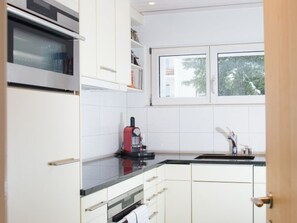 Une cuisine moderne avec des meubles blancs, un plan de travail noir, une machine à café rouge et une fenêtre donnant sur des arbres.