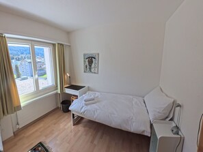 A small, tidy room with a bed, a desk, and a window with curtains. - Apartment  by Interhome (Lenzerheide)
