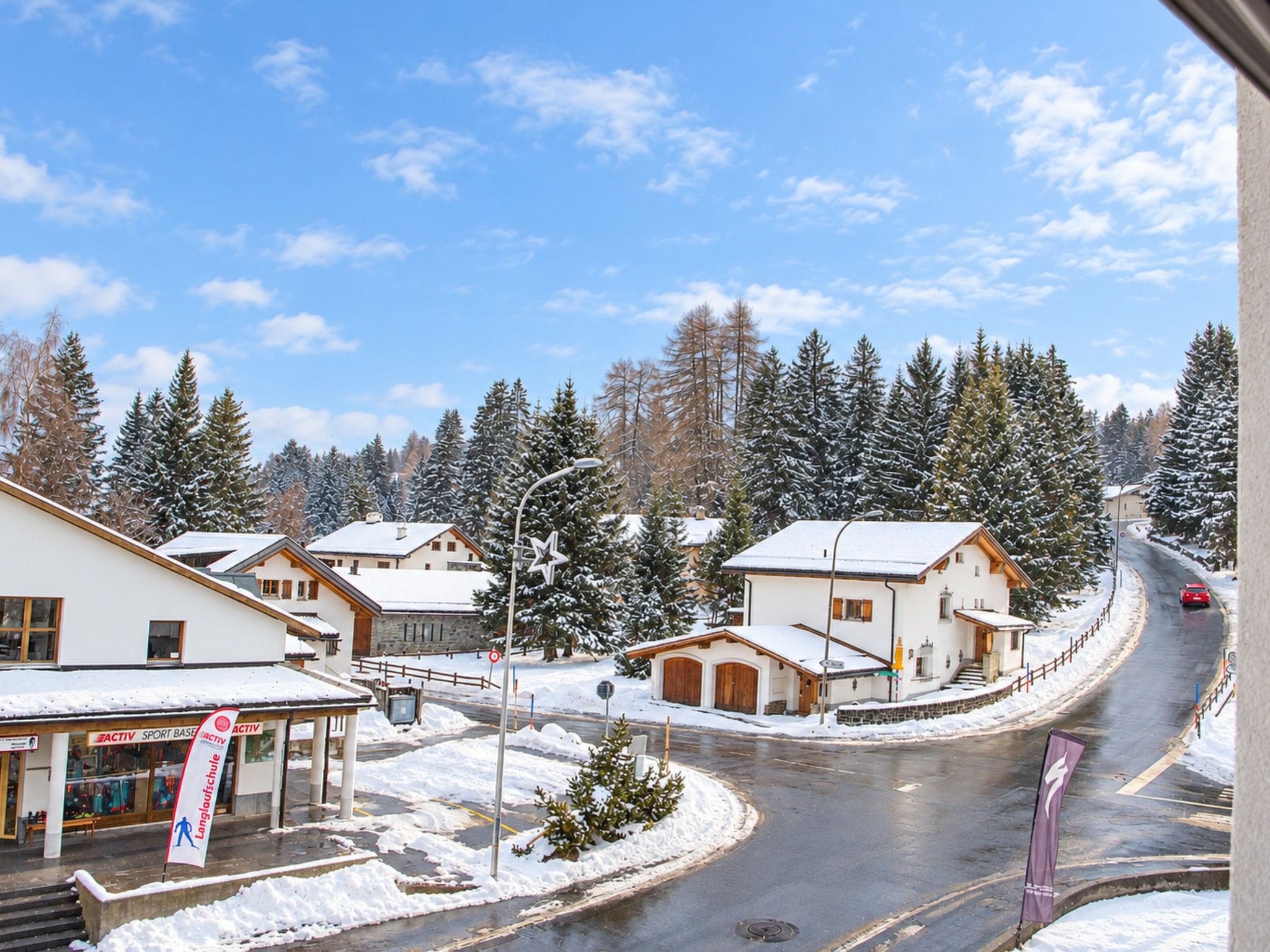 Un village enneigé, avec des bâtiments, une route et un ciel dégagé.