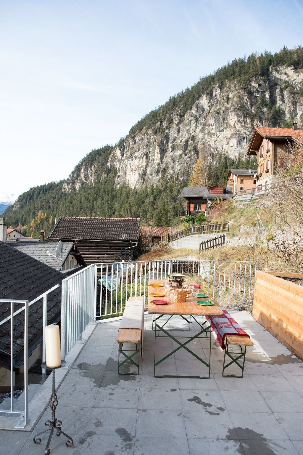 A terrace with a table set for dining, overlooking a mountainous landscape.