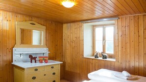 A wooden cabin room with a bed, a dresser, a mirror, and a window.