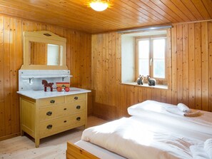 A wooden cabin room with a bed, a dresser, a mirror, and a window.