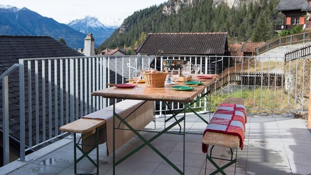 Un espacio de comedor al aire libre con una mesa y bancos, con vistas a un paisaje montañoso.