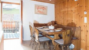 A dining area with a wooden table and chairs, a painting on the wall, and a view of the outside.