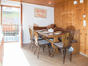 A dining area with a wooden table and chairs, a painting on the wall, and a view of the outside.