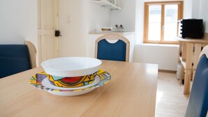 A dining table with a bowl and saucer, a blue chair, a wooden cabinet, and a window with a view.