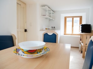 A dining table with a bowl and saucer, a blue chair, a wooden cabinet, and a window with a view.