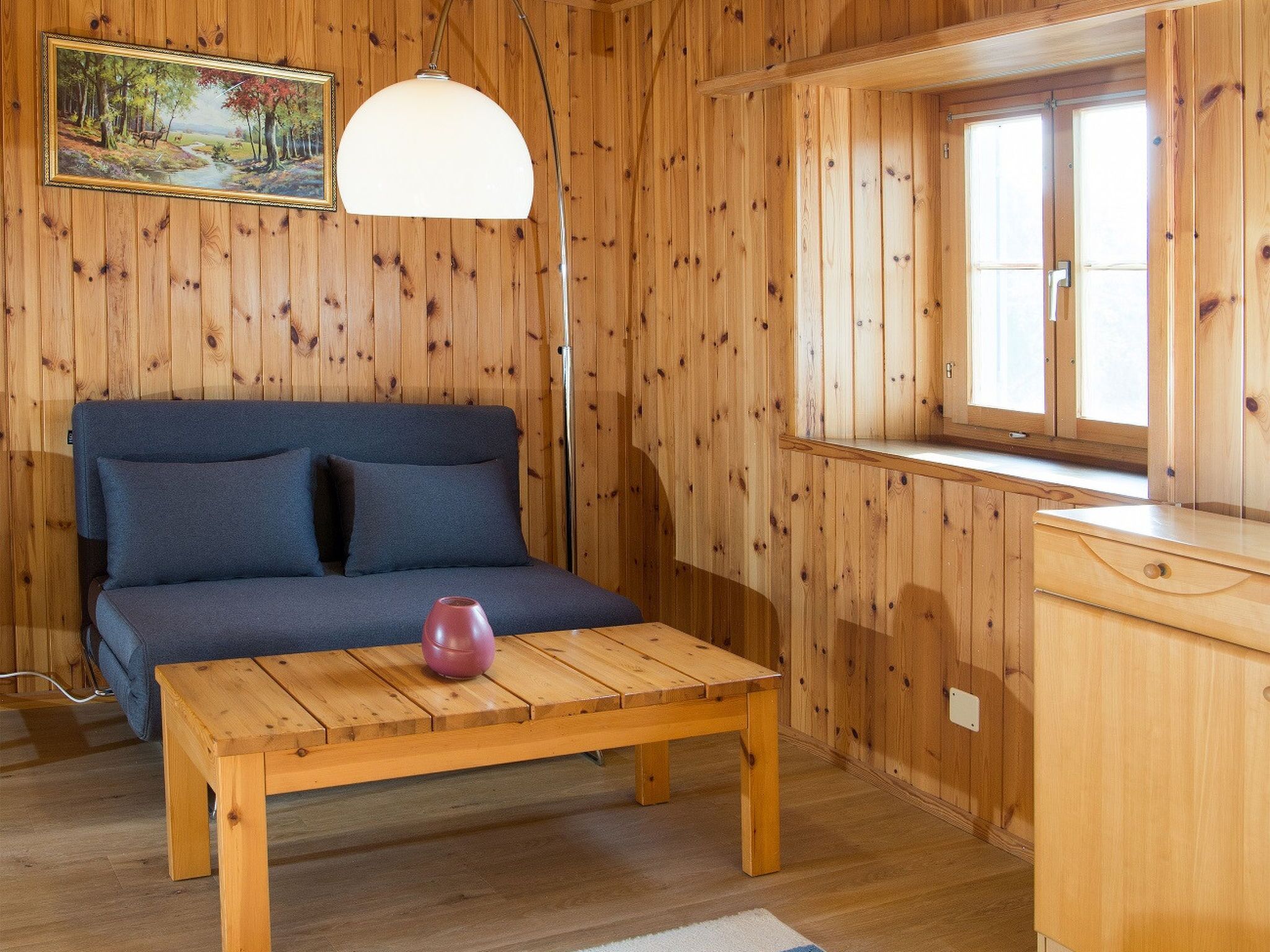 Un intérieur en bois avec un canapé, une table, une lampe et une fenêtre.