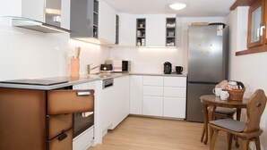 A compact kitchen with white cabinets, a built-in oven, a microwave, and a refrigerator. There's a small dining area with a wooden table and chairs.