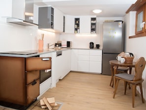 A compact kitchen with white cabinets, a built-in oven, a microwave, and a refrigerator. There's a small dining area with a wooden table and chairs.