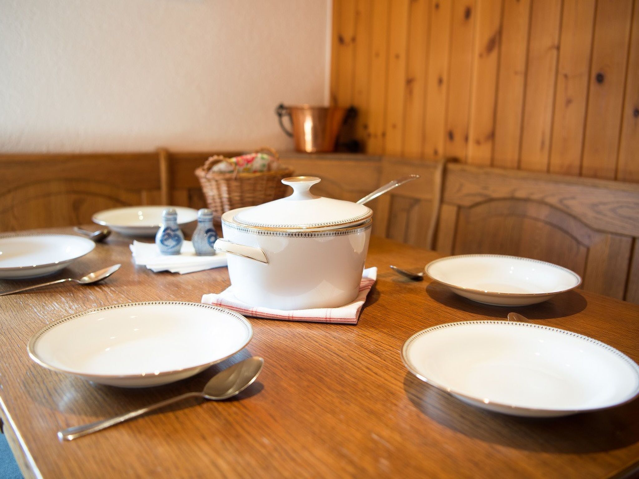 Une table de salle à manger en bois, avec des assiettes blanches, un pot à soupe et une cuillère.