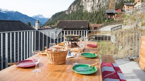 Mesa de comedor al aire libre con vista a la montaña, rodeada por una barandilla de metal.
